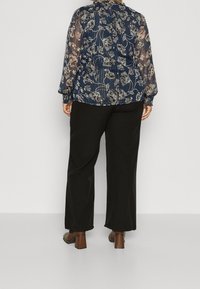 Blusa floreale blu navy in materiale trasparente e con polsini smock, abbinata a pantaloni neri a gamba larga e scarpe con tacco blocco marroni.