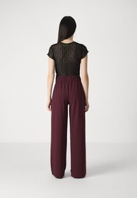 Czarny top z koronką i krótkimi rękawami, zestawiony z wysokimi spodniami o szerokich nogawkach w odcieniu bordowym, z elastycznym pasem i gładkim materiałem.