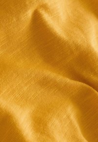 Tissu tricoté jaune doux avec texture visible et plis délicats créant des ombres et des reflets subtils.