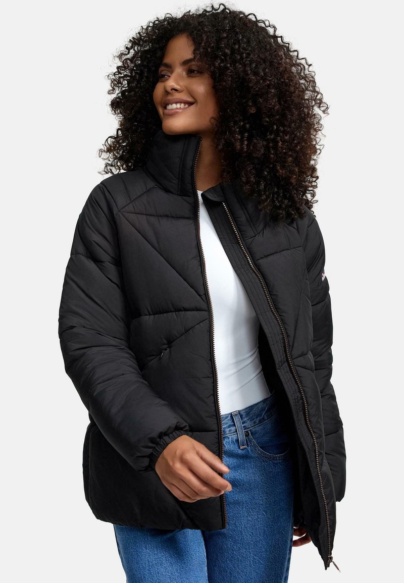 Sort polstret jakke med høj krave, prydet med diagonale quiltede mønstre og en frontlynlås. Bæres over en hvid top og blå jeans.