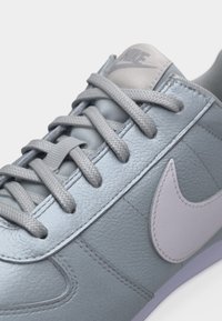 Κοντινή όψη ενός γκρι αθλητικού παπουτσιού Nike με υφή δέρματος, γκρι κορδόνια και λευκό λογότυπο Nike στο πλάι.