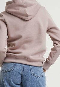 Sudadera con capucha en color rosa claro, hecha de una tela suave, con puños y dobladillo acanalados, combinada con jeans de tiro alto en azul.