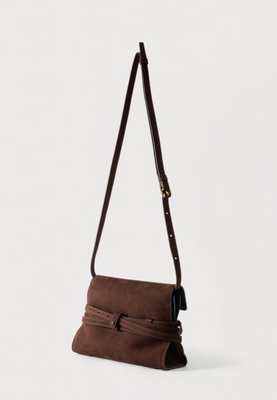 Bruine suède schoudertas met een verstelbare band en een omwikkelde ceintuurelement, geplaatst tegen een effen witte achtergrond.