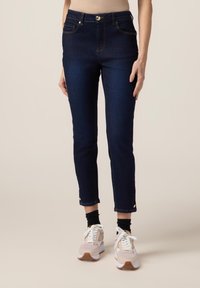 Jeans alti in denim blu scuro con una vestibilità slim, caratterizzati da cuciture arancioni, tasche frontali e orli alla caviglia con piccoli bottoni dorati.