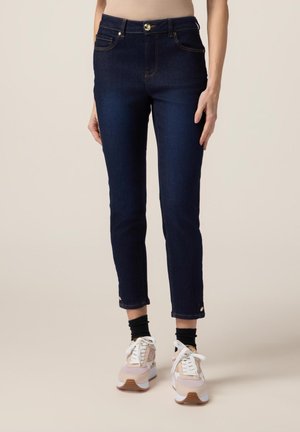 Jeans alti in denim blu scuro con una vestibilità slim, caratterizzati da cuciture arancioni, tasche frontali e orli alla caviglia con piccoli bottoni dorati.