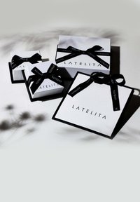 Quattro scatole regalo impilate in bianco con dettagli neri. Ognuna ha un nastro nero legato attorno, con il nome del marchio "LATELITA".