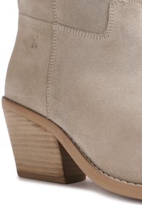 Bottine beige en daim avec talon bloc en bois empilé et détails de couture visibles.