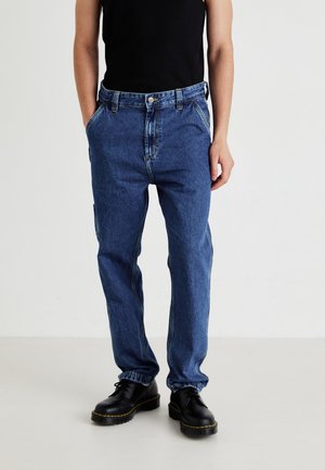Blue denim jeans with a straight design, five pockets, and visible stitching. Paired with black lace-up boots with yellow accents.