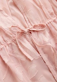 Tissu rose doux avec des motifs floraux texturés et un délicat nœud noué aux coutures froncées.
