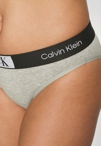Szürke pamut, bikini stílusú alsónemű fekete logós derékkal, amelyen a "Calvin Klein" felirat szerepel. Sima textúra és testhez simuló kialakítás.