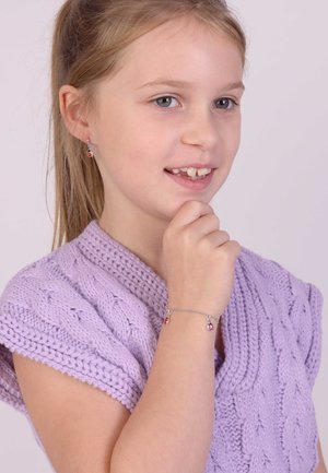 Paarse gebreide trui met een V-hals en kabelpatroon. Zilveren armband met twee kleurrijke bedels. Model heeft lang haar en zichtbare oorbellen.