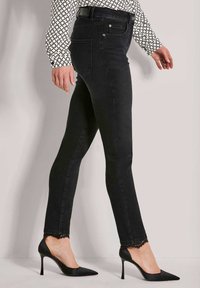 Zwarte denim jeans met een slanke pasvorm, voorzien van kanten rand aan de zoom, gecombineerd met puntige zwarte hakken en een blouse met geometrisch patroon.