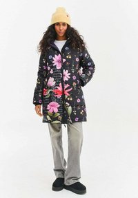 Květinový prošívaný kabát s černým pozadím, zdobený velkými růžovými a bílými květy. Zapínání na zip, s kapucí, kombinovaný se šedými džíny a černou obuví.