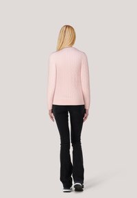 Helle rosa Strickpullover mit langen Ärmeln, mit gerippten Bündchen und Saum, kombiniert mit schwarzen Schlagjeans und sportlichem Schuhwerk.