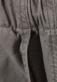 Tissu gris avec des rayures horizontales, présentant des coutures visibles le long de la ceinture élastique, offrant un aspect texturé.