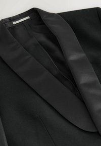 Black blazer with satin shawl collar, featuring a textured interior lining. Smooth fabric with a structured design and tailored fit.