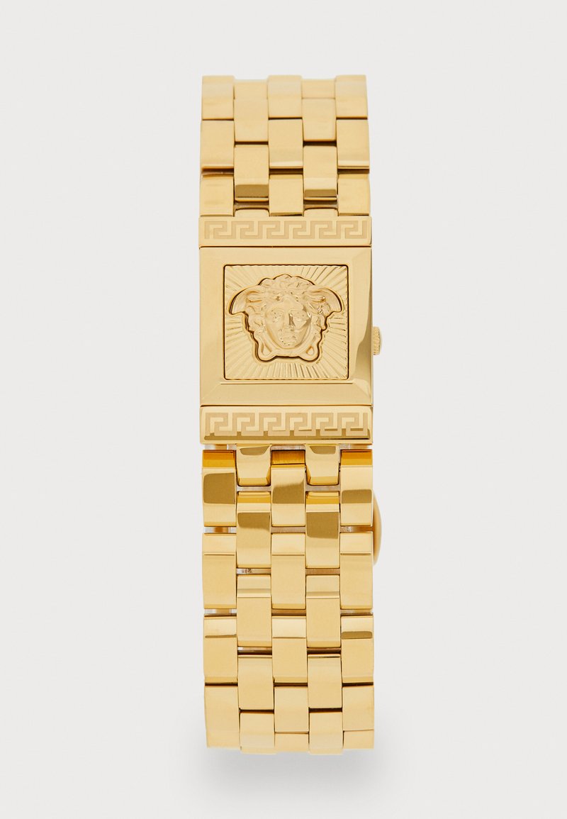 Relógio de pulso em tom dourado com uma face quadrada apresentando um motivo texturizado de cabeça de leão, design de bracelete ligado e acentos de chave grega.
