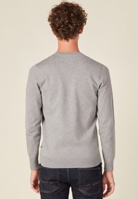 Maglione grigio a maglia con maniche lunghe, collo a giro e orlo a coste. Sembra morbido con una texture liscia, indossato sopra jeans scuri.