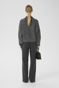 Grauer gestrickter Pullover mit hohem Kragen, kombiniert mit hoch taillierten schwarzen geraden Jeans. Hält eine kleine rechteckige grüne Tasche.