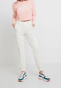 Rosa kortärmad sweatshirt med "Nike"-logotyp, vita smala cargobyxor med sidofickor och flerfärgade sportiga sneakers.