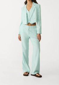 Blazer corta en color menta sobre un chaleco a juego y pantalones de pierna ancha, todos en una tela ligera; presenta botones y diseño frontal plano.