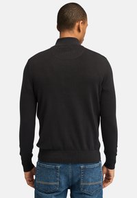 Sort trøje med stålkrave, ribbede manchetter og kant. Strikket tekstur, tætsiddende design og rene linjer. Båret sammen med blå denim jeans.