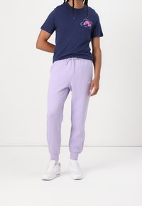 Námořnicky modré tričko s růžovým grafickým logem, doplněné světle fialovými tepláky a bílými teniskami. Měkká látka, volný střih, elastický pas.