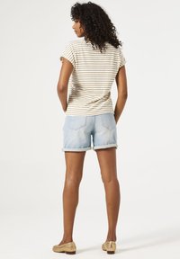 T-shirt rayé beige et blanc, manches courtes retroussées, assorti avec un short en jean bleu clair, porté avec les ourlets retroussés. Des chaussures en toile beiges complètent la tenue.