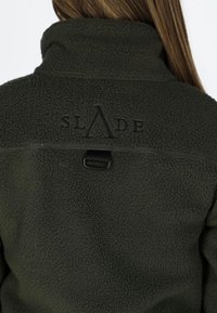 Fleecejack aan in donker groen met een hoge kraag. Bevat een geborduurd logo "SLADE" en een zwarte hardware accent op de achterkant.
