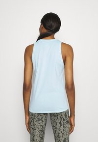 Vaaleansininen hihaton paita, joka on valmistettu pehmeästä kankaasta ja jossa on pyöreä kaula-aukko. Yhdistetty tummasävyisiin, vaaleilla yksityiskohdilla varustettuihin leggingsseihin.