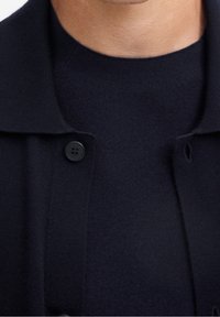 Navy knit pullover with a rounded neckline and a button closure near the collar. The fabric has a soft texture and a seamless design.
