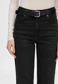Črne jeans hlače z visokim pasom, opremljene s pasom in črnim usnjenim pasom s srebrno pravokotno zaponko. Gladka tekstura.