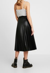 Gonna midi plissettata nera in ecopelle, abbinata a una maglietta bianca con pois. Modella in stivali alla caviglia neri con lacci.