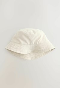 Krämfärgad bucket hat med en texturerad band, mjukt tyg och bred skärm. Har en rund krone och sömlös sömnad.