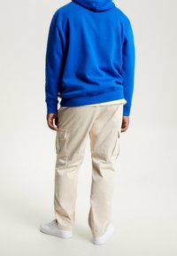 Felpa blu con cappuccio e coulisse, pantaloni cargo beige con tasche laterali e sneakers bianche. Tessuto morbido, vestibilità rilassata, design semplice.