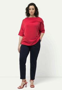 Top rojo de gran tamaño con escote drapeado, combinado con pantalones ajustados azul marino y tacones rojos con tiras. Tejido suave y diseño minimalista.