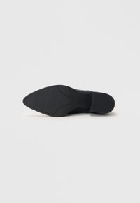 Sapato preto de salto alto com bico fino e textura suave. Apresenta uma sola de borracha detalhada com um padrão antiderrapante para maior aderência.