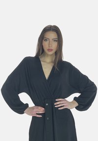 Vestito nero stile avvolgente con maniche lunghe a palloncino. Tessuto liscio con vita aderente e fronte con bottoni. Design minimalista.
