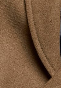 Brązowa tkanina z mieszanki wełny o miękkiej fakturze, z gładkim szwem i subtelnym połyskiem. Projekt zawiera detal w postaci złożonego kołnierza.