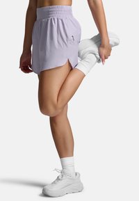 Lyselilla sportsshorts med elastisk talje, sideslidser og en lynlåslomme. Båret med hvide sneakers og ankelsokker.