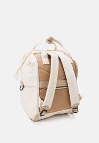 Vue arrière d'un sac à dos beige et marron clair avec des bretelles rembourrées, des poignées supérieures et une poche zippée, sur fond blanc.