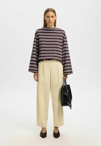 Triibuline, lõdvalt istuv tume- ja valge ülemine osa laia varrukaga, kombineeritud beežide kõrge vöökohaga pükstega ja musta käekotiga, mille küljes on triibuline sall.