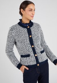 Cardigan lavorato a maglia con un motivo testurizzato blu navy e bianco, dotato di un colletto rotondo, tre bottoni dorati e due tasche frontali.