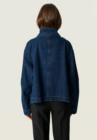 Dark blue denim jacket with a relaxed fit, classic collar, and dropped shoulder seams. Features simple stitching and a cropped hem.