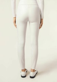 Vita, figurnära leggings med en slät textur. Har hög midja och avsmalnande ben, kombinerat med vita skor och en ljus topp.