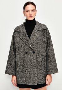 Cappotto a motivo pied de poule in bianco e nero, con ampio colletto, chiusura doppiopetto e maniche ampie. Tessuto testurizzato.