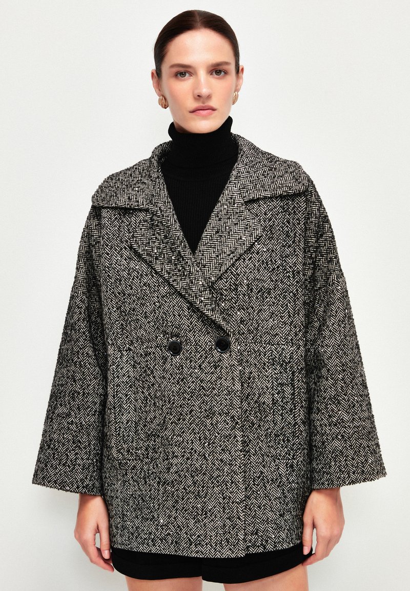 Cappotto a motivo pied de poule in bianco e nero, con ampio colletto, chiusura doppiopetto e maniche ampie. Tessuto testurizzato.