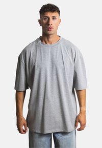 Šedé oversized tričko vyrobené z měkké tkaniny, s kulatým výstřihem, krátkými rukávy a volným střihem, spárované se světle modrými denimovými šortkami.