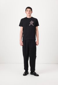 Zwarte katoenen t-shirt met een schuine witte en roze logo; losse zwarte broek; zwarte schoenen. Eenvoudig ontwerp met een minimalistische esthetiek.