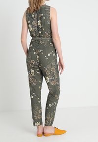 Mono floral en verde oscuro, con un diseño entallado en la cintura y sin mangas. Acentuado con un colorido patrón de flores y cinturilla elástica.